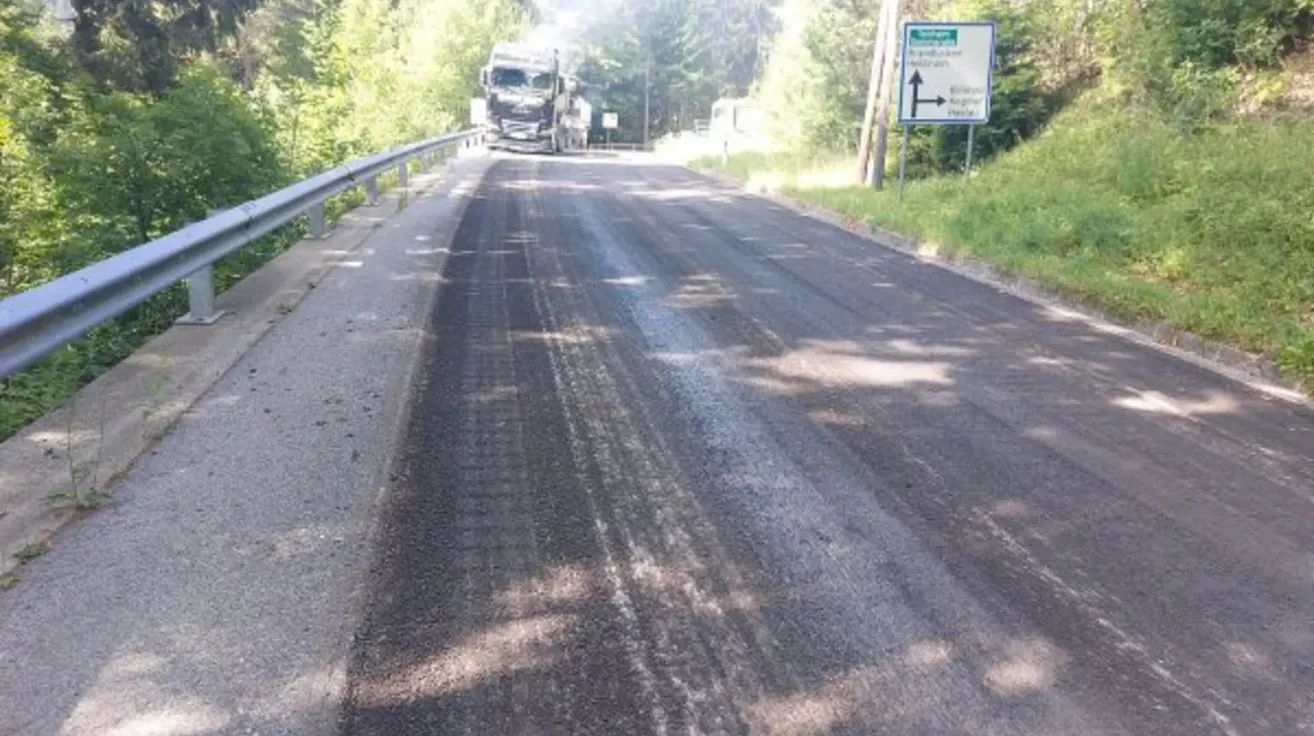 A road with a truck driving down it, fresh asphalt, and a sign indicating a right turn for trains.