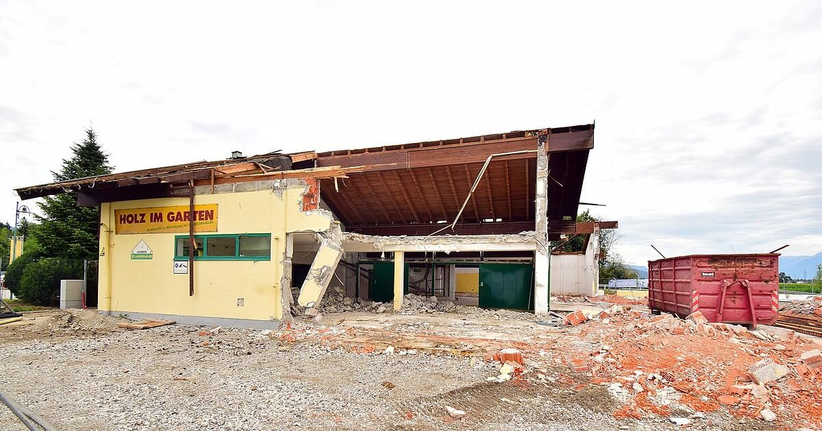 A yellow building with a sign reading 'M GARTEN' is under demolition. The roof is partially collapsed, and debris is scattered around. The building's front wall is mostly intact, with green doors and windows.