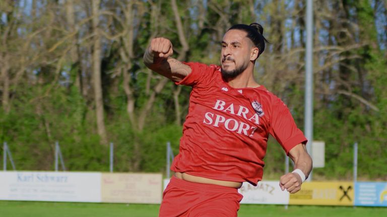 Ein Mann in einem roten Fußballtrikot mit dem Wort 'BARA SPORT' darauf läuft und hebt seine Faust.
