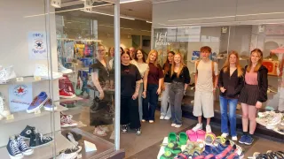 A group of people, possibly employees, are standing in front of a shoe store with a display of colorful shoes inside. The store has a glass door with the words 'I feel fashion' written on it.