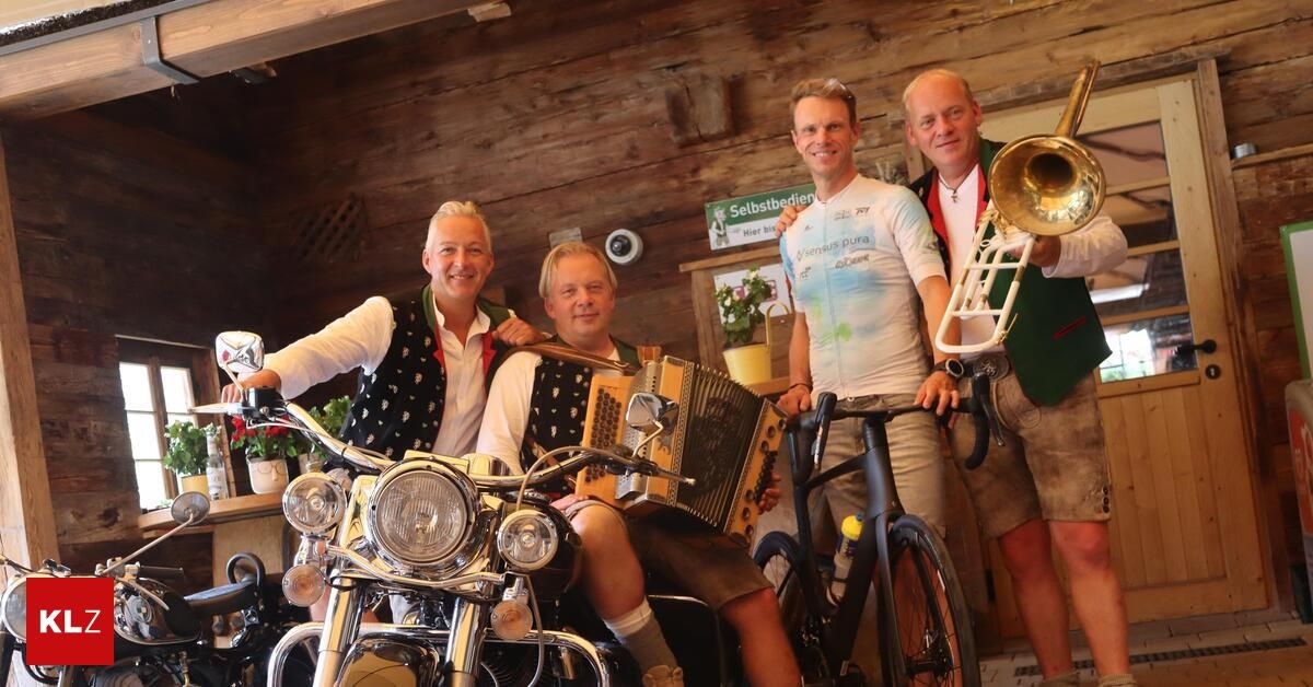 Four men are standing in a room with wooden walls, one playing an accordion, another holding a trombone, and the other two standing next to a motorcycle and a bicycle.