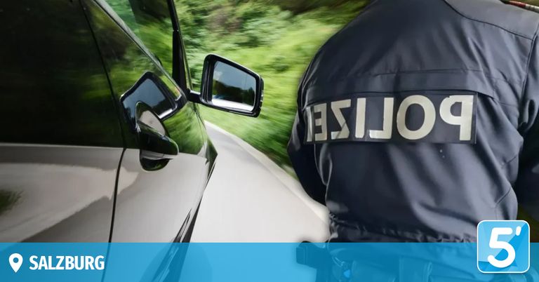 Ein Polizeibeamter in einer schwarzen Uniform steht neben einem Auto auf einer Straße, mit einem verschwommenen Hintergrund von Grün.