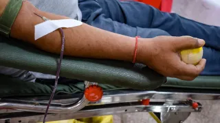 A person is lying on a stretcher, wearing a bracelet and a medical tube on their arm. The person's hand is resting on the armrest.