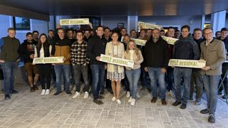 A group of people are posing for a photo while holding signs that say 'Immer Regional' and 'Erste Wahl'. They are smiling and standing in a line.