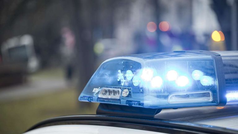 A close-up view of a police car's emergency lights, with blue lights flashing and the word Hella visible on the light bar.