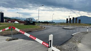 A construction site with a newly paved road, surrounded by mountains, with a machinery vehicle parked on the side.