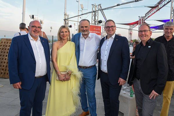 Fünf formell gekleidete Personen, die lächelnd für ein Foto auf einem Dach mit einer malerischen Aussicht auf die Stadt posieren.