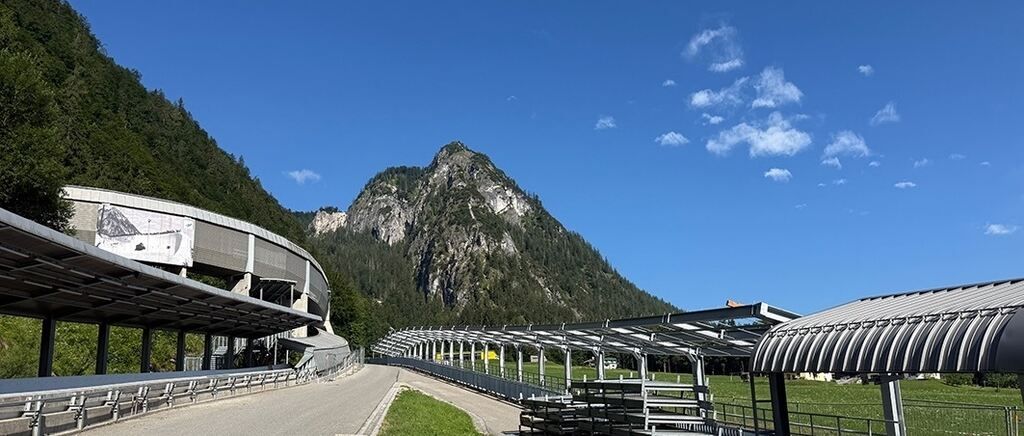 Ein malerisches Panorama eines Berges mit einer Straße, die zu einem Tunneleingang führt. Der Himmel ist klar mit einigen Wolken.