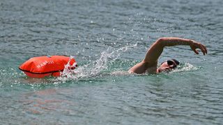 A man swims in a lake wearing goggles and a red floater with the word Nabu on it.