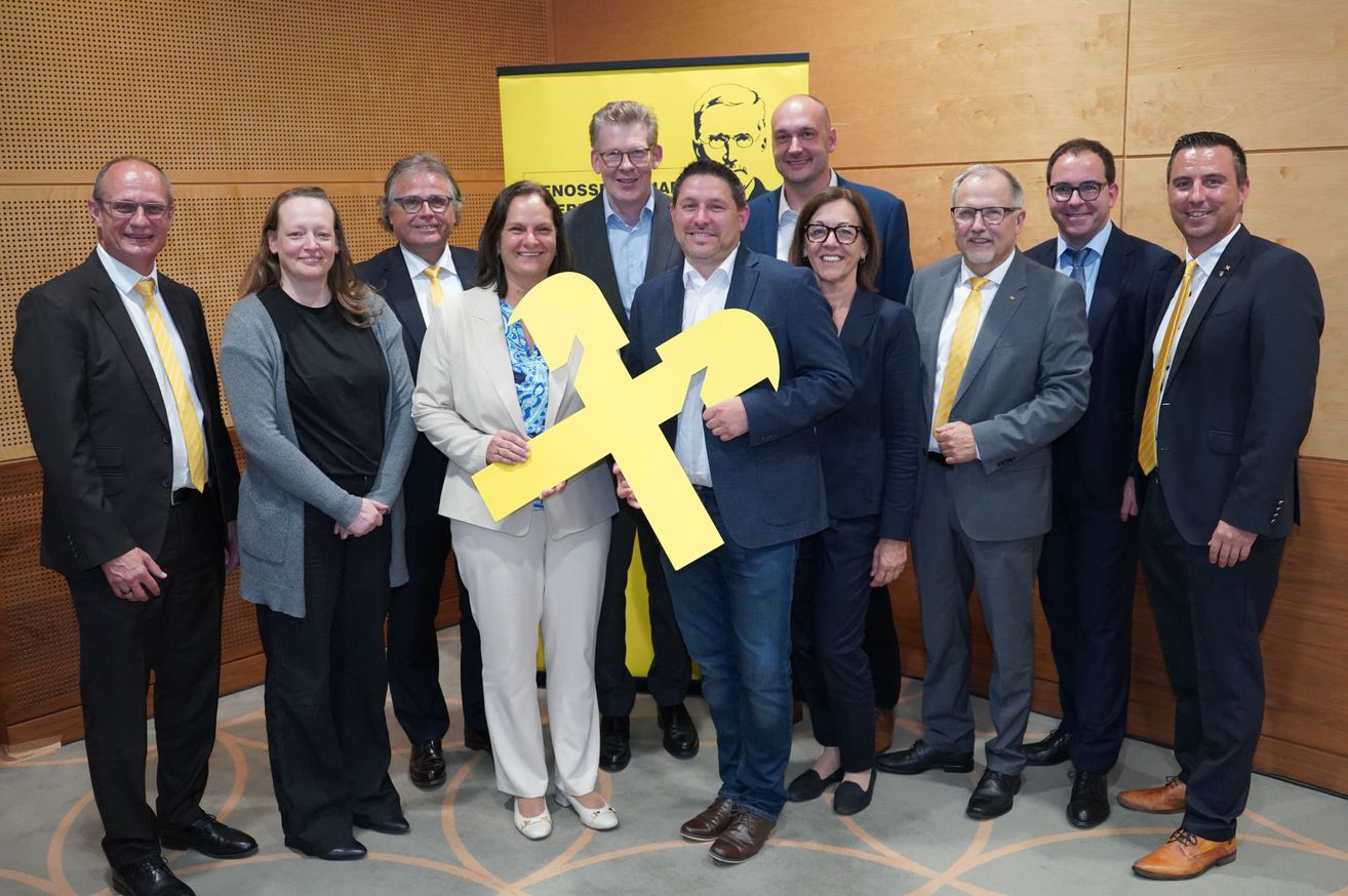 Eine Gruppe von Fachleuten in formeller Kleidung, die zusammenstehen, einer hält einen großen gelben Buchstaben F, mit einem gelben Banner im Hintergrund.