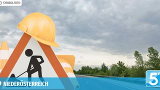 A road sign with a construction worker silhouette and a yellow hard hat on top, against a cloudy sky and a blurred road.