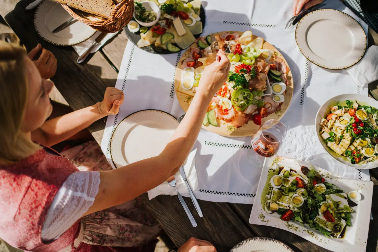 A table set with various dishes including meats, vegetables, and eggs. A person is reaching for a slice of meat with a knife.