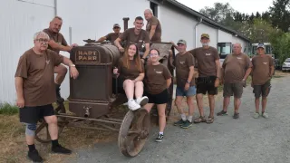 A group of people wearing brown shirts are posing for a photo in front of an old tractor.