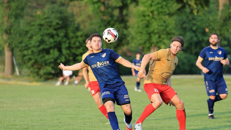Ein Fußballspieler in einem blauen Trikot mit dem Wort 'Zeilinger' köpft den Ball, während ein anderer Spieler in einem gelben Trikot mit der Nummer '15' verteidigt.