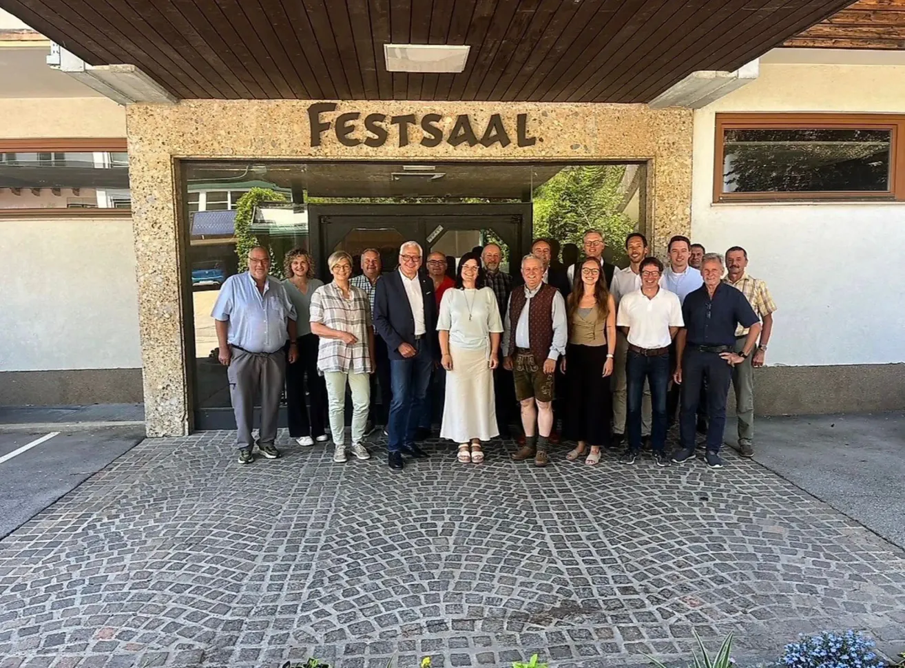 A group of people are posing for a photo in front of a building with the name Festsaal. They are standing on a cobblestone floor.