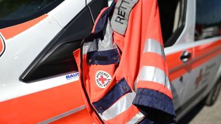 Eine orange Sicherheitsjacke mit reflektierenden Streifen und dem Wort Rettung auf dem Rücken hängt an der Tür eines Rettungswagens.