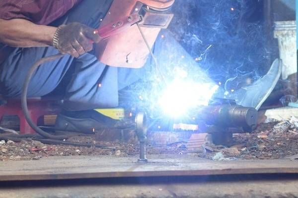 A man wearing a welding mask welds a metal pipe on a metal surface.