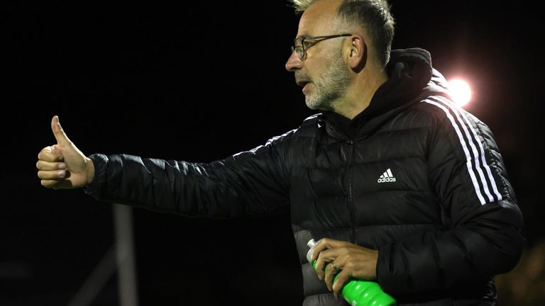 Ein Mann in einer schwarzen Adidas-Jacke gestikuliert mit der Hand und hält eine grüne Wasserflasche.
