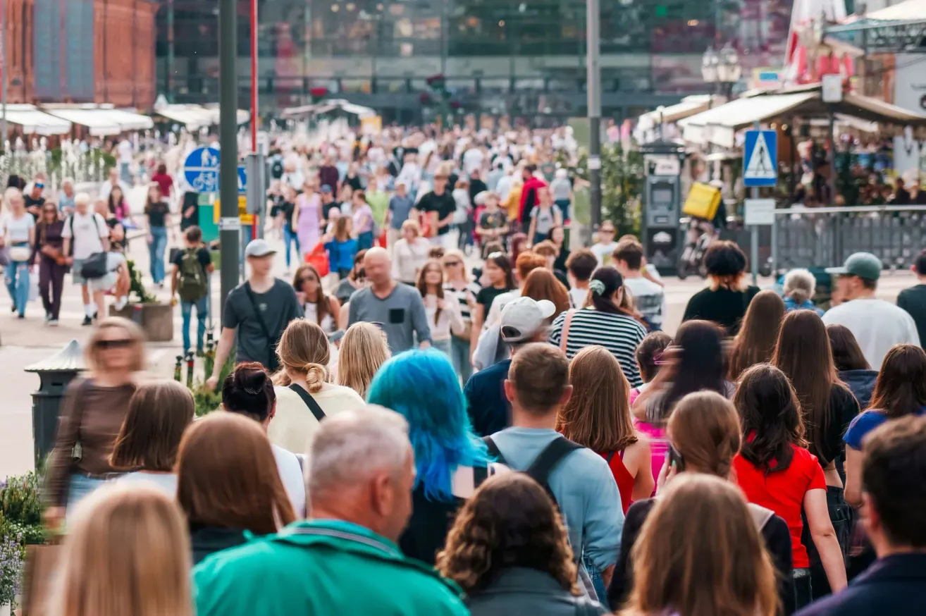 Eine geschäftige Stadtstraße voller Menschen, die gehen, einige tragen Hüte und tragen Taschen, mit Gebäuden und Straßenlaternen im Hintergrund.