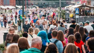 Eine geschäftige Stadtstraße voller Menschen, die gehen, einige tragen Hüte und tragen Taschen, mit Gebäuden und Straßenlaternen im Hintergrund.