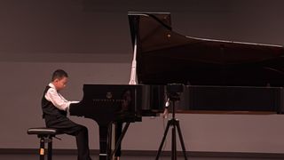 Ein junger Junge spielt ein Steinway & Sons Konzertflügel auf der Bühne, mit einem Stativ und einer Kamera in der Nähe.