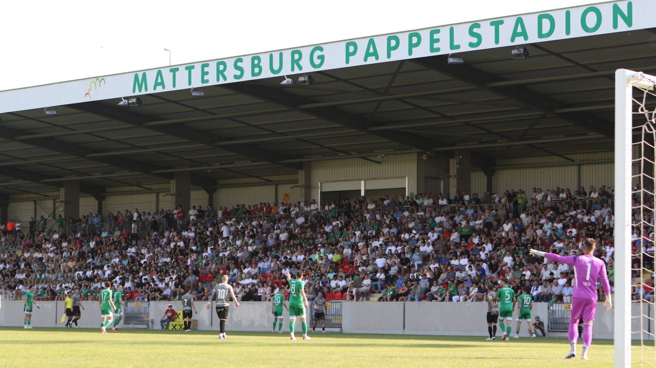 Fußballspieler in grünen Trikots laufen auf dem Feld vor einem großen Publikum im Mattersburg Pappelstadion.
