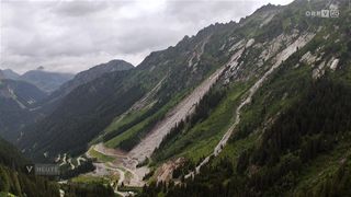Ein Berg mit einem Bergrutsch am Hang, mit einer Straße im Tal darunter.