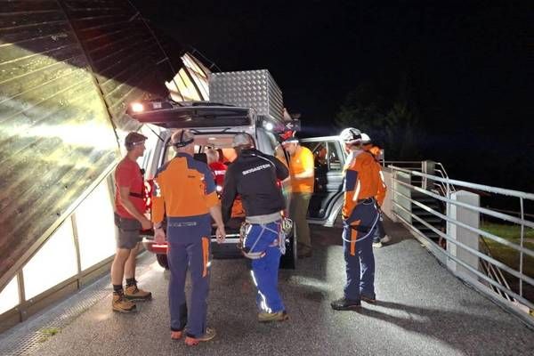 Eine Gruppe von Personen in Sicherheitsausrüstung steht um ein Fahrzeug mit offenem Kofferraum auf einer Brücke bei Nacht.