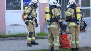 Eine Gruppe von Feuerwehrleuten in voller Ausrüstung, einschließlich Helmen und Sauerstoffflaschen, steht vor einem Gebäude.