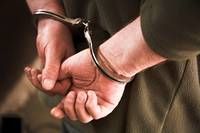Eine Person in Handschellen hält ihre Hände zusammen, möglicherweise in einem Polizeirevier.