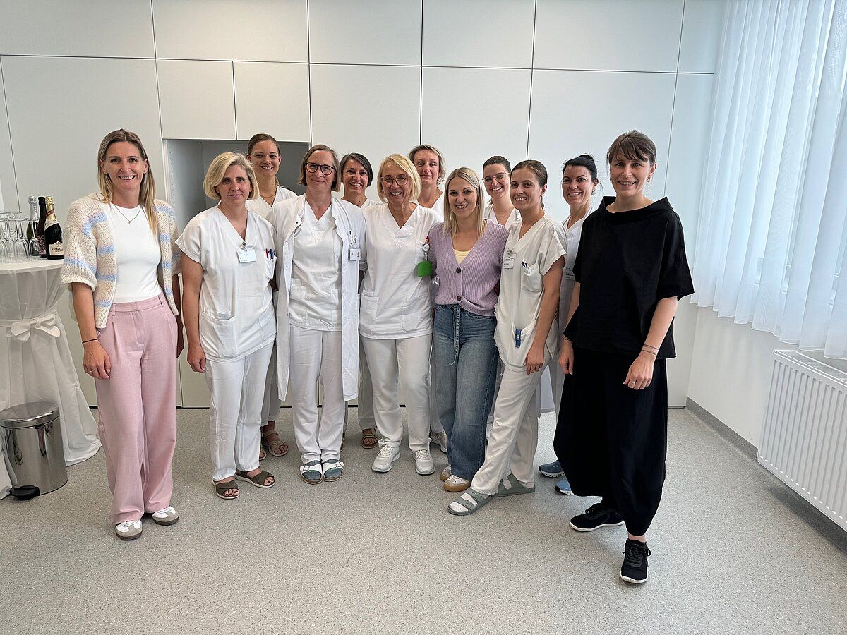 Eine Gruppe von Frauen, einige in weißen Uniformen, posiert für ein Foto in einem Krankenhauskorridor.