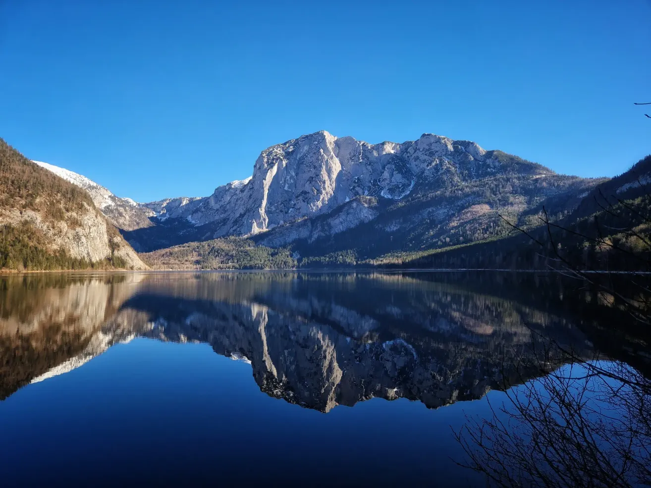 Eine ruhige Berglandschaft mit klarem blauem Himmel und einem ruhigen See, der die Berge und Bäume widerspiegelt.