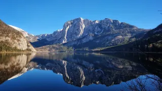 Eine ruhige Berglandschaft mit klarem blauem Himmel und einem ruhigen See, der die Berge und Bäume widerspiegelt.