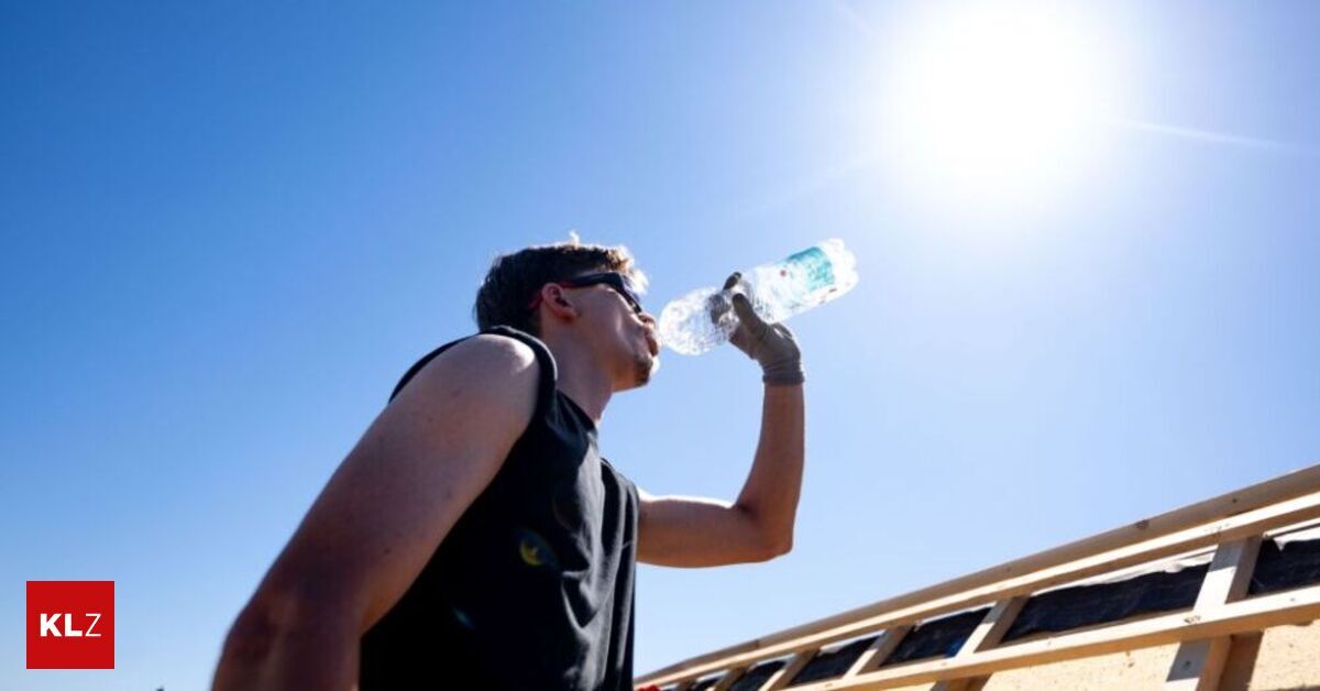 Ein Mann trinkt Wasser aus einer Flasche, während er auf einer Holzkonstruktion unter einem klaren blauen Himmel steht.