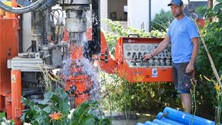 Ein Mann bedient eine große orange Bohrmaschine in einem Garten und spritzt Wasser, während sie bohrt.