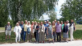 Eine Gruppe von Menschen, einige mit Sonnenbrillen, stehen vor einem Baum an einem sonnigen Tag. Sie lächeln und scheinen für ein Foto zu posieren.