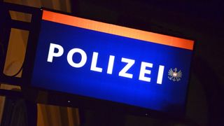 Ein blaues Schild mit dem Wort 'POLIZEI' in weißer Schrift, das das österreichische Wappen auf der rechten Seite zeigt. Das Schild ist gegen einen dunklen Hintergrund beleuchtet.