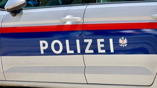 Eine Nahaufnahme der Seite eines Polizeiwagens mit dem Wort 'POLIZEI' in Weiß auf blauem Hintergrund, mit einem weißen Emblem auf der rechten Seite.