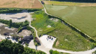 Eine Luftaufnahme einer Baustelle mit Baumaschinen und Reifenhaufen. Die Baustelle ist von grünen Feldern und einer unbefestigten Straße umgeben.