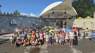 Eine Gruppe von Kindern und Erwachsenen posiert für ein Foto vor einer burgartigen Bühne mit weißem Vordach. Die Bühne hat ein Schild mit der Aufschrift Ritterrost Arena.