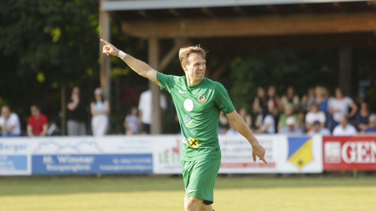 Ein Fußballspieler in einem grünen Trikot feiert auf dem Spielfeld und zeigt in den Himmel.