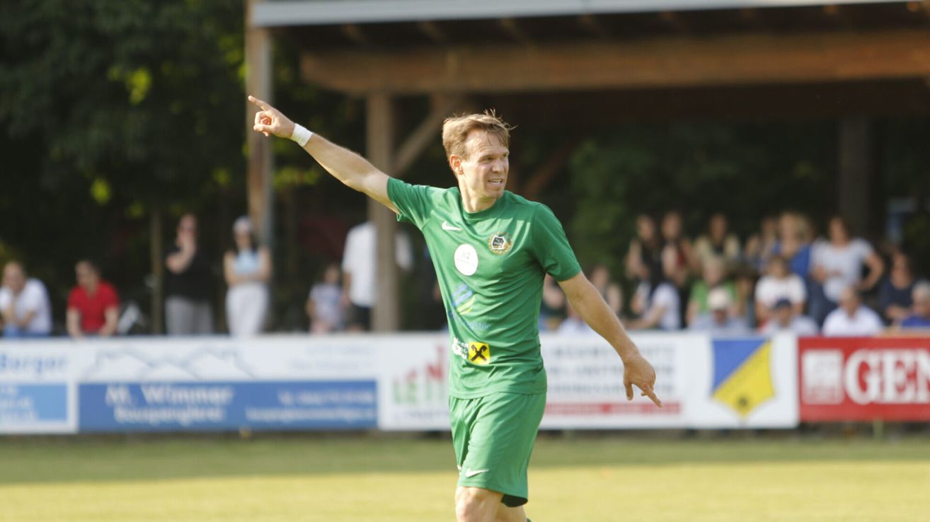 Ein Fußballspieler in einem grünen Trikot feiert auf dem Spielfeld und zeigt in den Himmel.