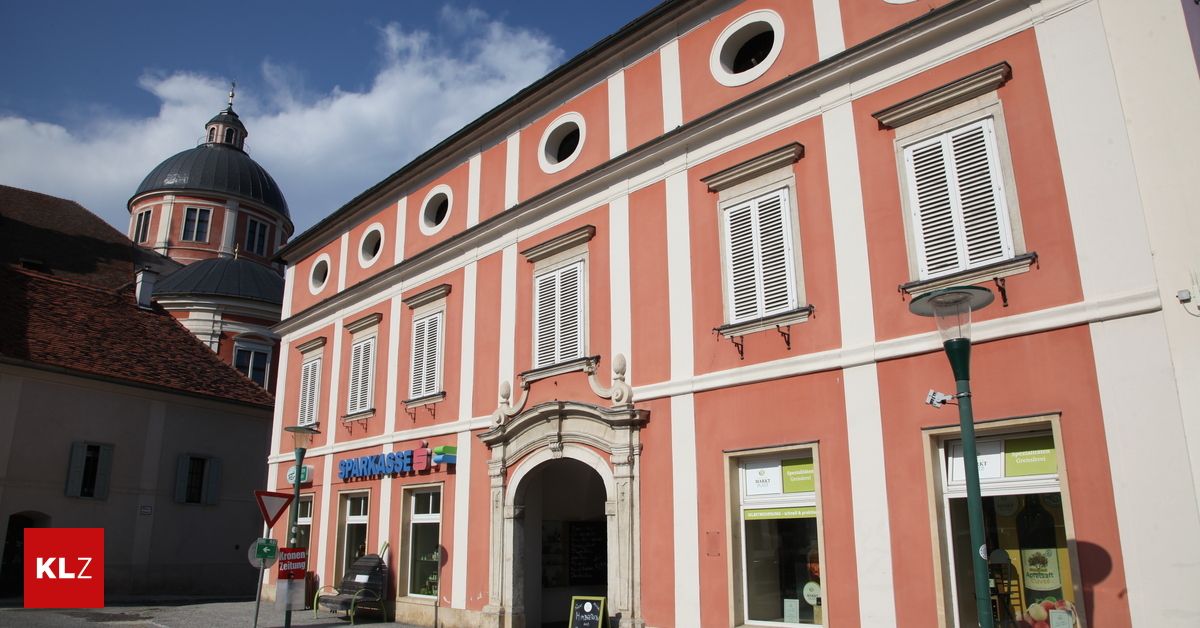 Ein rosafarbenes Gebäude mit weißen Fensterläden und einem großen Bogeneingang, mit einem Schild über ihm, das 'Sparkasse' steht.