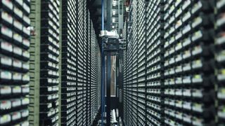 Ein langer Korridor in einem Rechenzentrum mit Reihen von Server-Racks auf beiden Seiten, ein Roboterarm ist zwischen den Racks zu sehen.