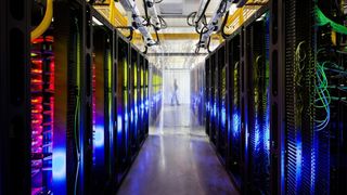 Ein Serverraum gefüllt mit Reihen von Server-Racks, beleuchtet mit blauen und gelben Lichtern, mit einer Person in der Ferne stehend.