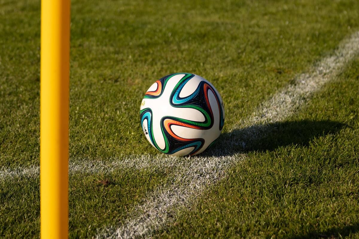 Ein Fußball mit leuchtenden, mehrfarbigen Mustern liegt auf einem gut gepflegten Rasenfeld in der Nähe einer Grenzlinie.