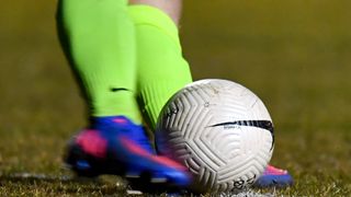 Der Fuß eines Fußballspielers in neongrünen Socken und blauen Stollenschuhen ist positioniert, um einen weißen Fußball mit schwarzen und weißen Mustern zu schießen.