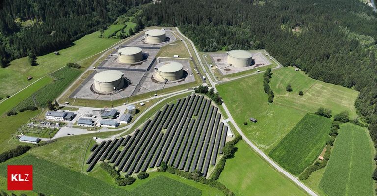 Luftaufnahme eines Solarparks mit großen Speichertanks in einem ländlichen Gebiet, umgeben von Bäumen und Feldern.
