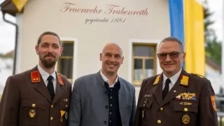 Drei Männer in Uniformen stehen vor einem Gebäude mit einem Schild, das 'Feuerwehr Trabenreith gegründet 1881' besagt. Der Mann links hat einen Bart, der mittlere Mann ist kahl und der rechte Mann trägt eine Brille.