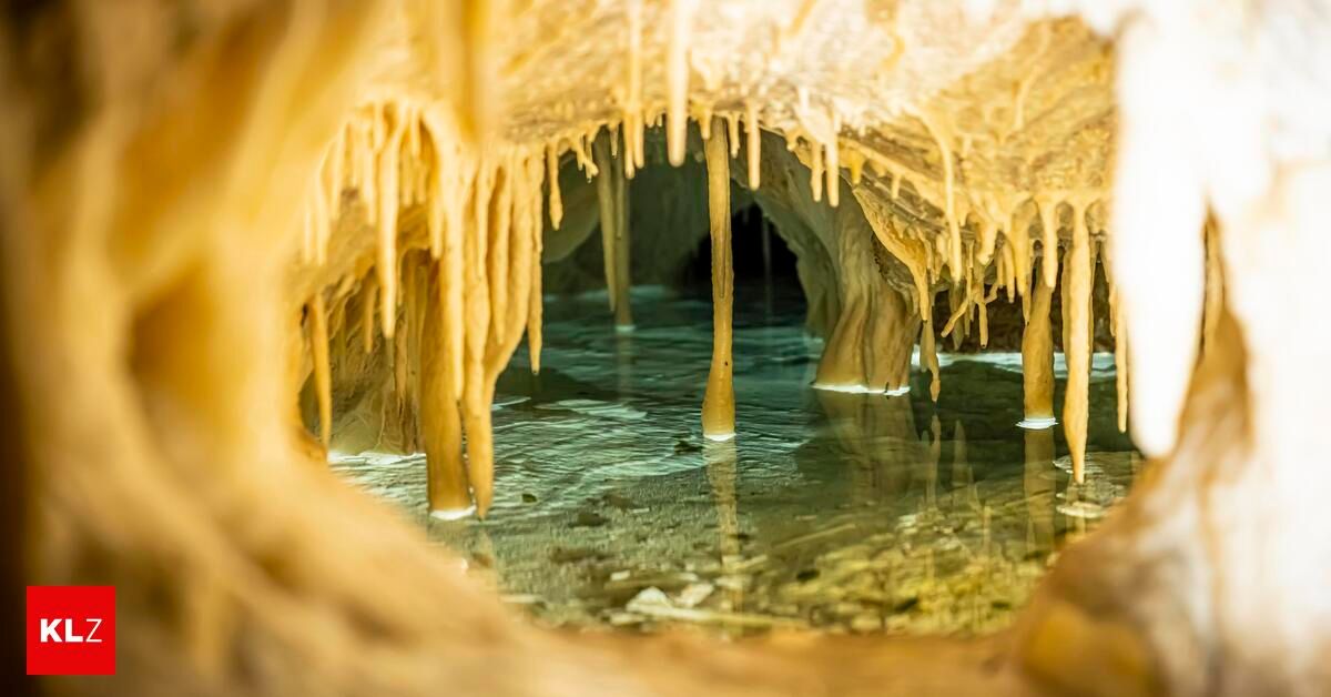 Eine Höhle mit Stalaktiten und Stalagmiten, die von einem sanften Licht beleuchtet werden, zeigt klares Wasser und Mineralablagerungen.